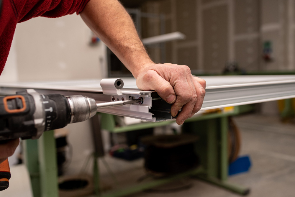 A close-up of a person using a power drill to assemble or repair a section of a garage door or metal frame in a workshop.