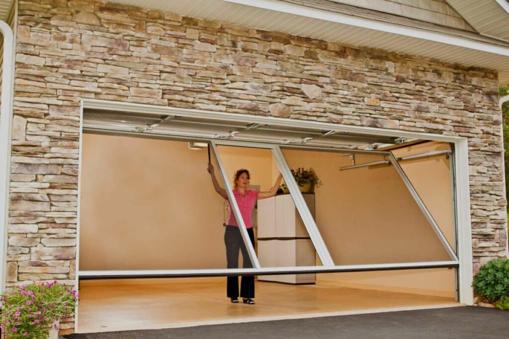 A person lifting an overhead garage door in a residential stone-faced garage.